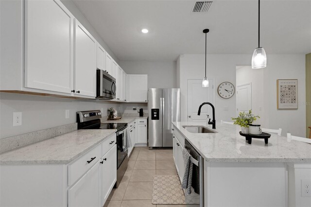 kitchen with appliances with stainless steel finishes, a sink, an island with sink, white cabinets, and light tile patterned floors