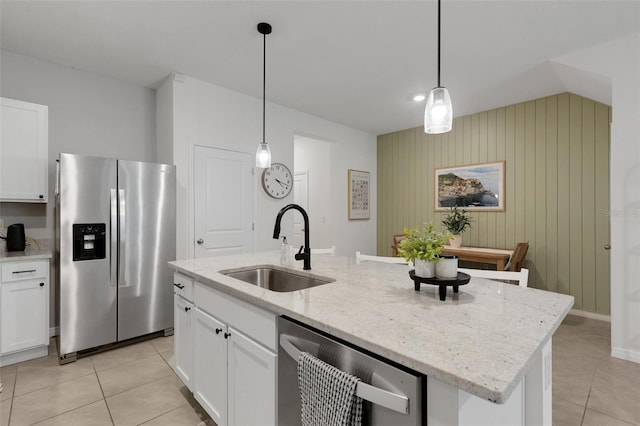 kitchen featuring appliances with stainless steel finishes, a sink, light tile patterned floors, white cabinets, and wooden walls