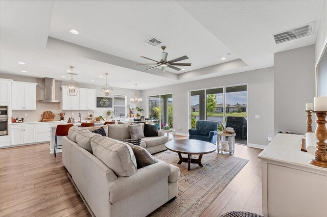 1017 Fernleaf Run, Bradenton, FL 34212 - living room featuring a tray ceiling, a ceiling fan, recessed lighting, light wood-style flooring, and a chandelier