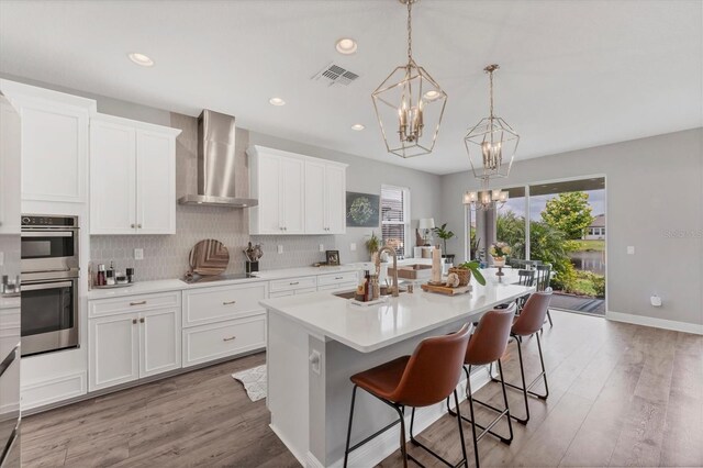 1017 Fernleaf Run, Bradenton, FL 34212 - kitchen with wall chimney range hood, a chandelier, stainless steel double oven, black electric stovetop, and light countertops
