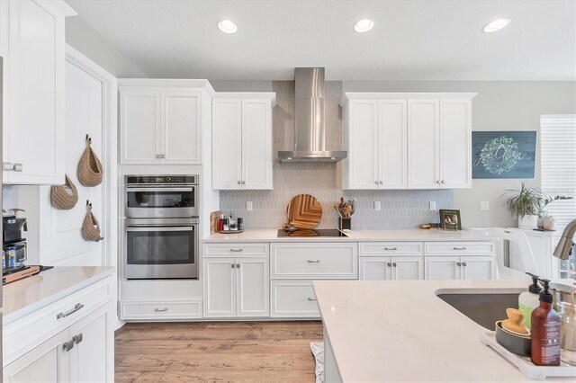 1017 Fernleaf Run, Bradenton, FL 34212 - kitchen with wall chimney range hood, stainless steel double oven, white cabinets, black electric stovetop, and light wood-type flooring