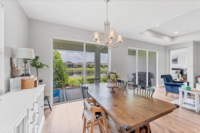 1017 Fernleaf Run, Bradenton, FL 34212 - dining area featuring light wood-style flooring, a chandelier, a raised ceiling, and a water view