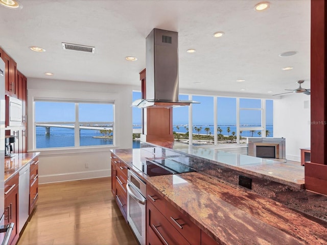 226 Golden Gate Pt Unit 63, Sarasota, FL 34236 - kitchen featuring island exhaust hood, black electric stovetop, stainless steel oven, baseboards, and light wood-style floors