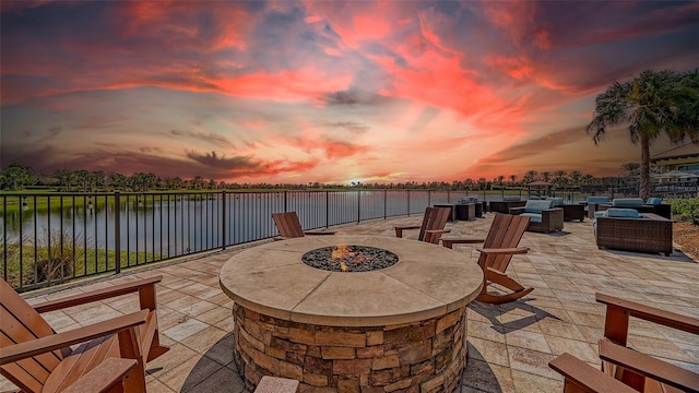 patio terrace at dusk with an outdoor fire pit, a water view, and fence