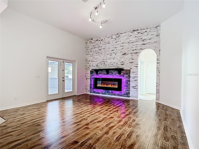 4239 Corso Venetia Blvd, Venice, FL 34293 - unfurnished living room featuring wood finished floors, a glass covered fireplace, arched walkways, baseboards, and french doors