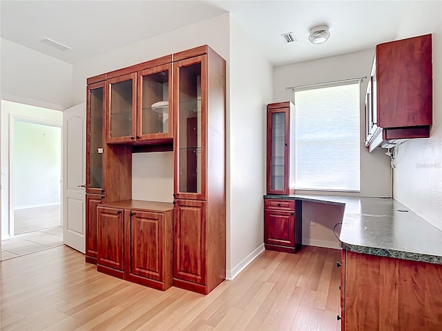 4239 Corso Venetia Blvd, Venice, FL 34293 - kitchen featuring light wood finished floors, glass insert cabinets, dark countertops, and baseboards
