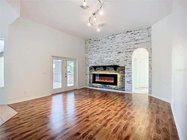 4239 Corso Venetia Blvd, Venice, FL 34293 - unfurnished living room featuring wood finished floors, arched walkways, a stone fireplace, baseboards, and track lighting