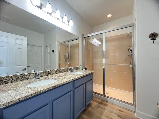 bathroom featuring a shower stall, wood finished floors, and double vanity