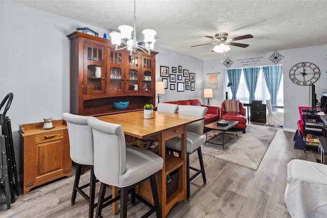 dining area featuring a chandelier, a textured ceiling, a ceiling fan, and light wood-style flooring