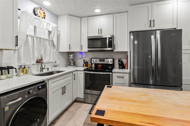 kitchen featuring washer / dryer, stainless steel appliances, a sink, white cabinetry, and backsplash