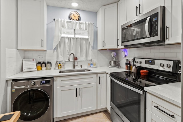kitchen featuring washer / dryer, stainless steel appliances, a sink, white cabinetry, and backsplash