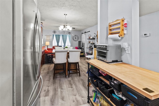 kitchen with freestanding refrigerator, a chandelier, light wood-style floors, butcher block counters, and a textured ceiling