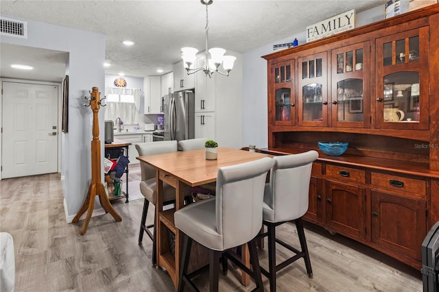 dining room featuring a chandelier, light wood-type flooring, a textured ceiling, and recessed lighting