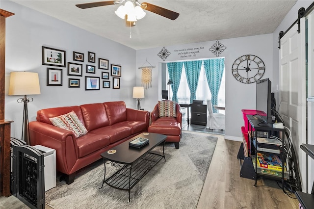 living area with a barn door, wood finished floors, a ceiling fan, baseboards, and a textured ceiling