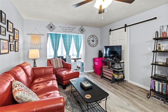 living area with wood finished floors, a ceiling fan, a barn door, baseboards, and a textured ceiling