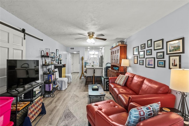 living area featuring wood finished floors, a ceiling fan, a barn door, a textured ceiling, and a chandelier