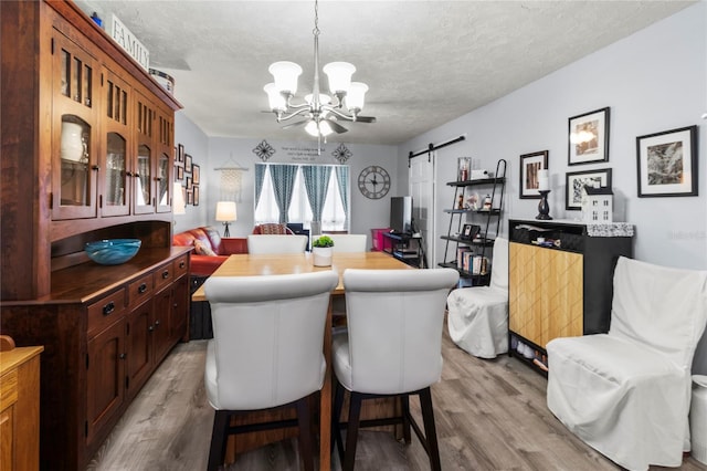 4189 Heron Way Unit 406E, Bradenton, FL 34205 - dining space featuring a chandelier, light wood finished floors, a barn door, and a textured ceiling