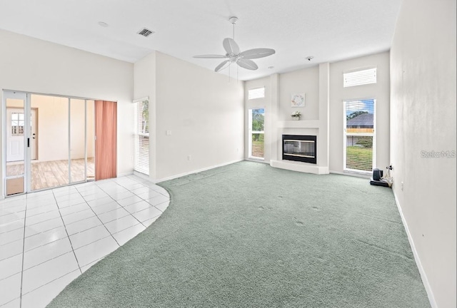 unfurnished living room featuring carpet floors, ceiling fan, baseboards, a glass covered fireplace, and tile patterned floors