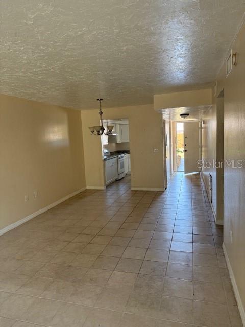 7273 Cloister Dr Unit 121, Sarasota, FL 34231 - unfurnished room with a textured ceiling, baseboards, a chandelier, and light tile patterned flooring