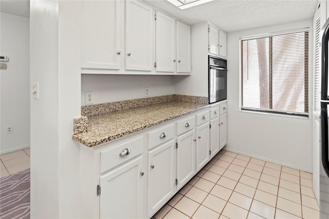 7500 40th Ave W Unit 108, Bradenton, FL 34209 - kitchen featuring oven, a textured ceiling, white cabinetry, light tile patterned flooring, and light stone countertops