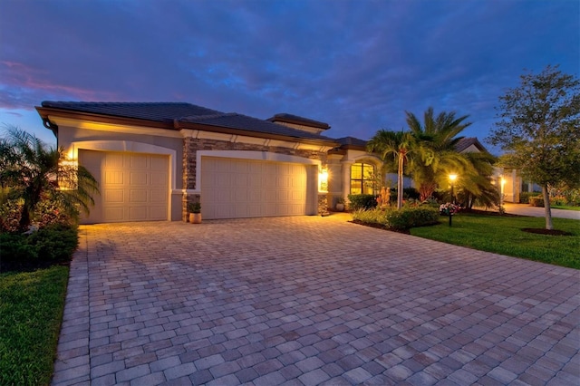 view of front of property featuring decorative driveway, an attached garage, a front yard, and stucco siding