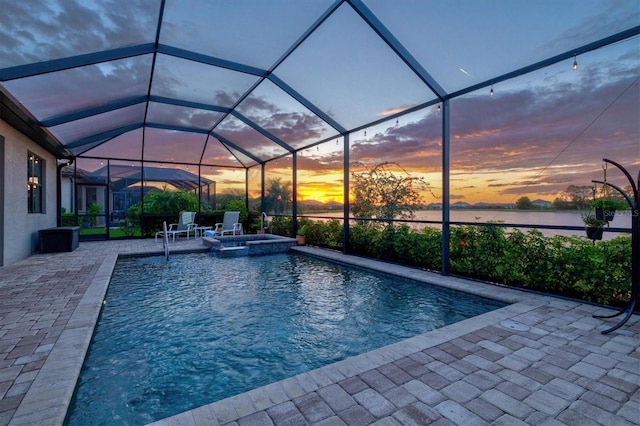 pool at dusk with a water view, a patio area, a pool with connected hot tub, and glass enclosure