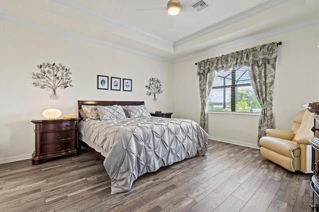 bedroom with a raised ceiling, wood finished floors, crown molding, baseboards, and a ceiling fan