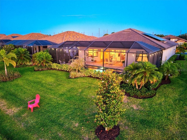 back of house featuring a lawn, glass enclosure, and a patio