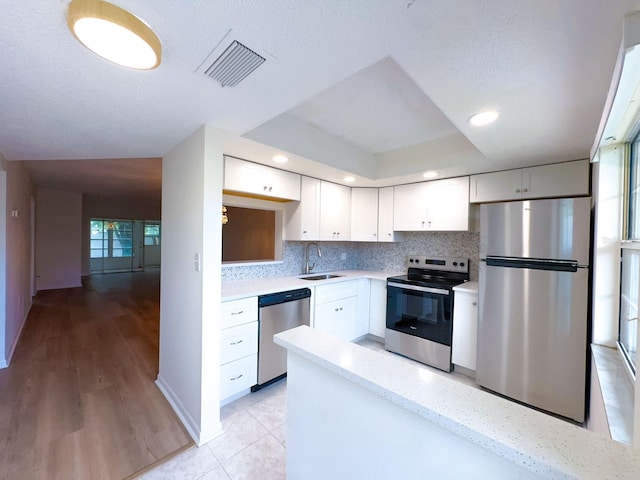 kitchen featuring appliances with stainless steel finishes, a sink, white cabinets, backsplash, and recessed lighting