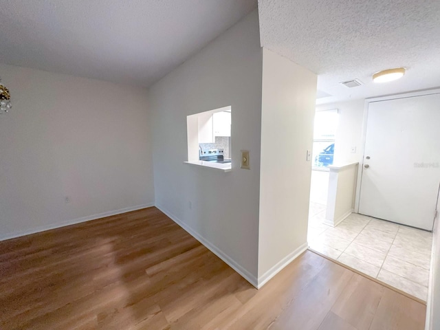 unfurnished room with light wood-type flooring, baseboards, and a textured ceiling