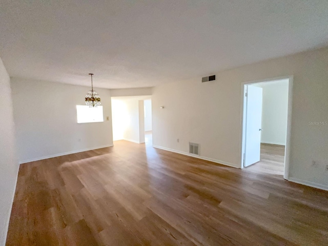 empty room with a chandelier, wood finished floors, and baseboards