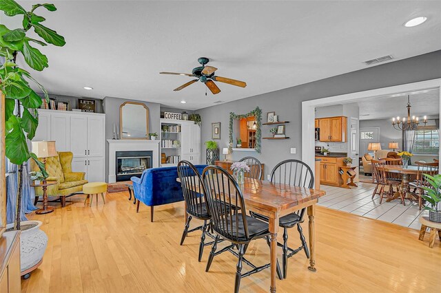 2708 27th Avenue Dr W, Bradenton, FL 34205 - dining area featuring a glass covered fireplace, light wood finished floors, a ceiling fan, a chandelier, and recessed lighting