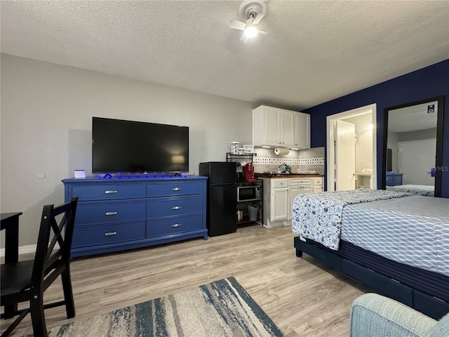 bedroom featuring freestanding refrigerator, light wood-style floors, and a textured ceiling