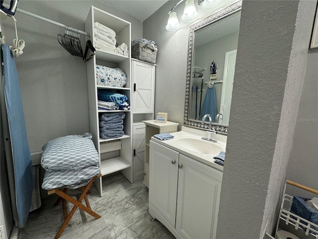 full bathroom featuring marble look tile flooring, a textured wall, vanity, and a spacious closet