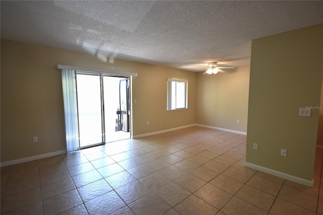 spare room featuring a textured ceiling, light tile patterned flooring, a ceiling fan, and baseboards
