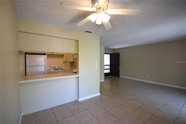 kitchen featuring freestanding refrigerator, a textured ceiling, tile patterned floors, a sink, and ceiling fan