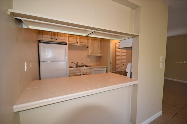 kitchen featuring white appliances, a sink, tile patterned floors, baseboards, and a peninsula