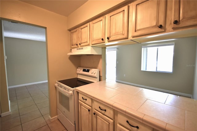 kitchen featuring white range with electric cooktop, under cabinet range hood, tile counters, light tile patterned flooring, and baseboards