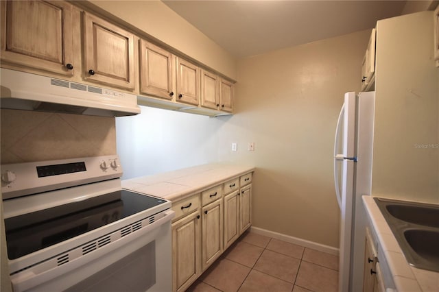 kitchen featuring white appliances, under cabinet range hood, light tile patterned flooring, baseboards, and a sink