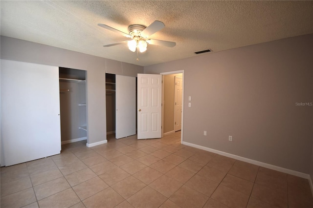unfurnished bedroom featuring two closets, a textured ceiling, light tile patterned flooring, a ceiling fan, and baseboards