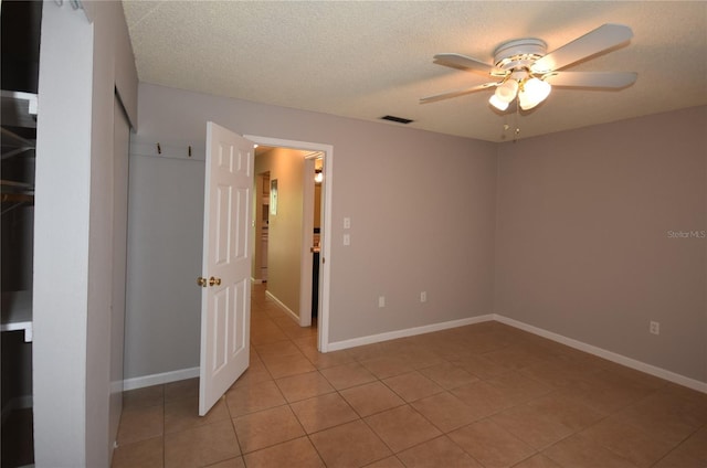 unfurnished bedroom with light tile patterned floors, a closet, baseboards, a ceiling fan, and a textured ceiling