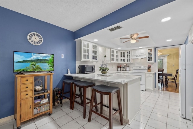 6207 Courtside Dr Unit 23, Bradenton, FL 34210 - kitchen featuring white appliances, under cabinet range hood, a peninsula, a breakfast bar area, and light stone counters
