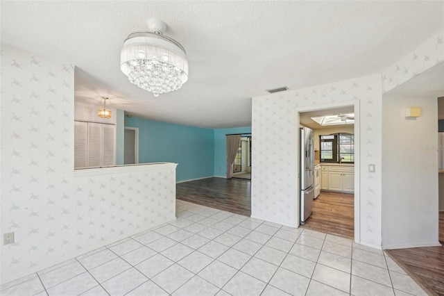 104 Hourglass Dr, Venice, FL 34293 - spare room featuring wallpapered walls, a chandelier, a textured ceiling, baseboards, and light tile patterned floors