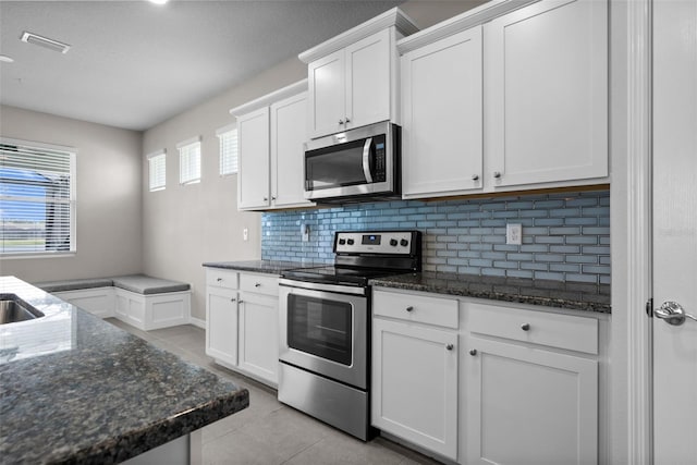 kitchen with stainless steel appliances, light tile patterned flooring, backsplash, and dark stone countertops