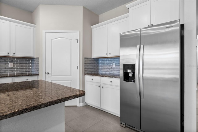 kitchen with stainless steel fridge, dark stone countertops, white cabinets, and backsplash