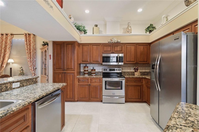 4804 Jacaranda Heights Dr, Venice, FL 34293 - kitchen with appliances with stainless steel finishes, tasteful backsplash, light stone counters, light tile patterned floors, and brown cabinetry