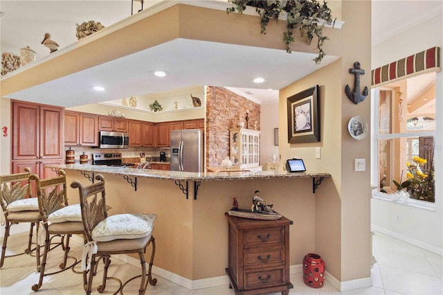 4804 Jacaranda Heights Dr, Venice, FL 34293 - kitchen featuring stainless steel appliances, a breakfast bar area, light stone counters, a peninsula, and brown cabinets