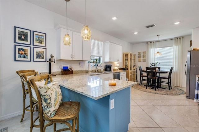 kitchen featuring white cabinets, stainless steel appliances, a sink, a peninsula, and light stone countertops