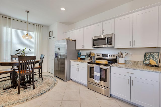 kitchen with stainless steel appliances, white cabinetry, decorative light fixtures, light tile patterned floors, and light stone counters