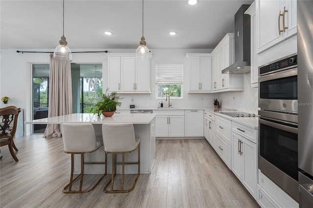 5651 Trevesta Pl, Palmetto, FL 34221 - kitchen featuring wall chimney range hood, healthy amount of natural light, stainless steel double oven, a kitchen breakfast bar, and recessed lighting
